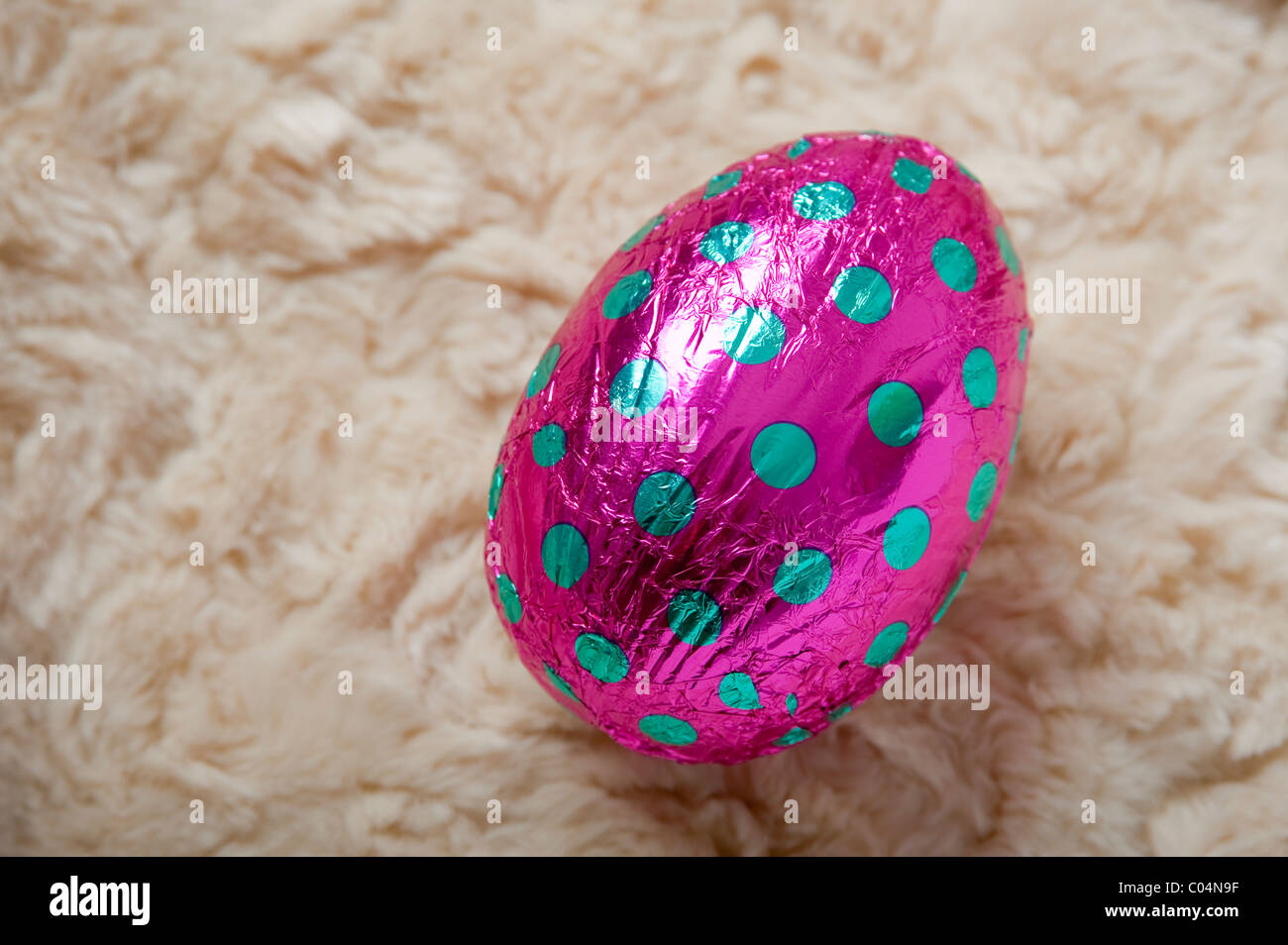 Seul gros oeuf de pâques en chocolat emballé dans rose avec des taches turquoise aluminium à un angle sur une toison de laine crème background Banque D'Images