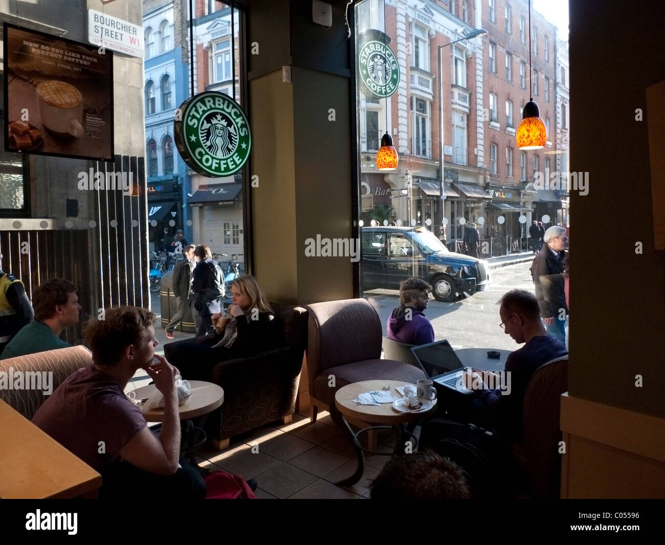 Les clients de l'intérieur Starbucks assis dans le salon buvant du café et de l'homme à l'aide d'un ordinateur portable à Soho Londres Angleterre Royaume-Uni KATHY DEWITT Banque D'Images