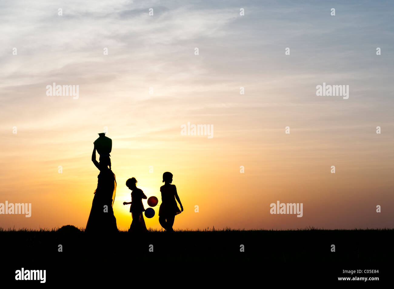 Mère indienne portant de l'eau pot avec des enfants et des ballons dans la campagne indienne. Silhouette Banque D'Images