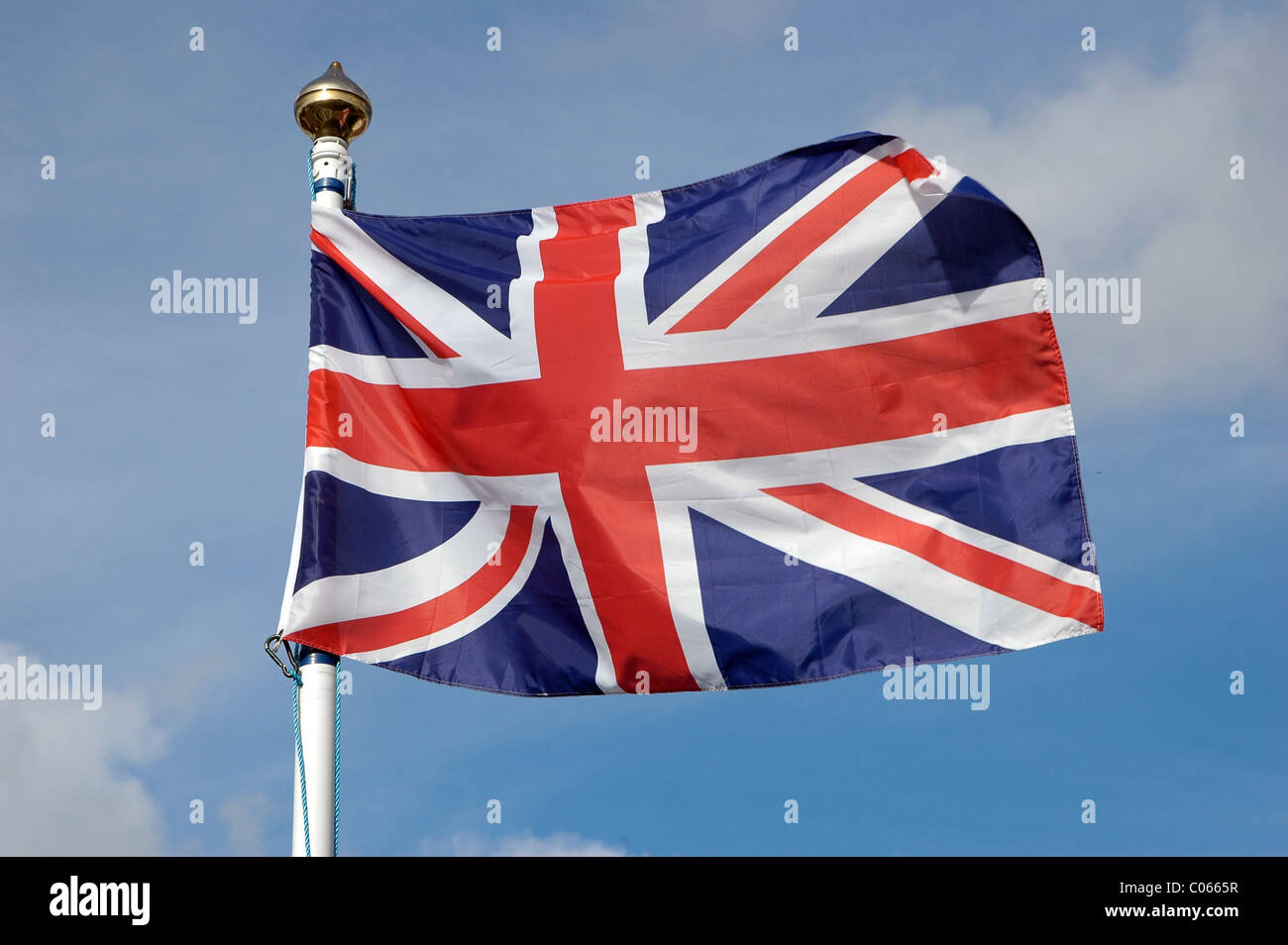 Un drapeau de l'union ou 'Union Jack' battant sur un mât dans un pays britannique village contre un ciel bleu avec des nuages. Banque D'Images