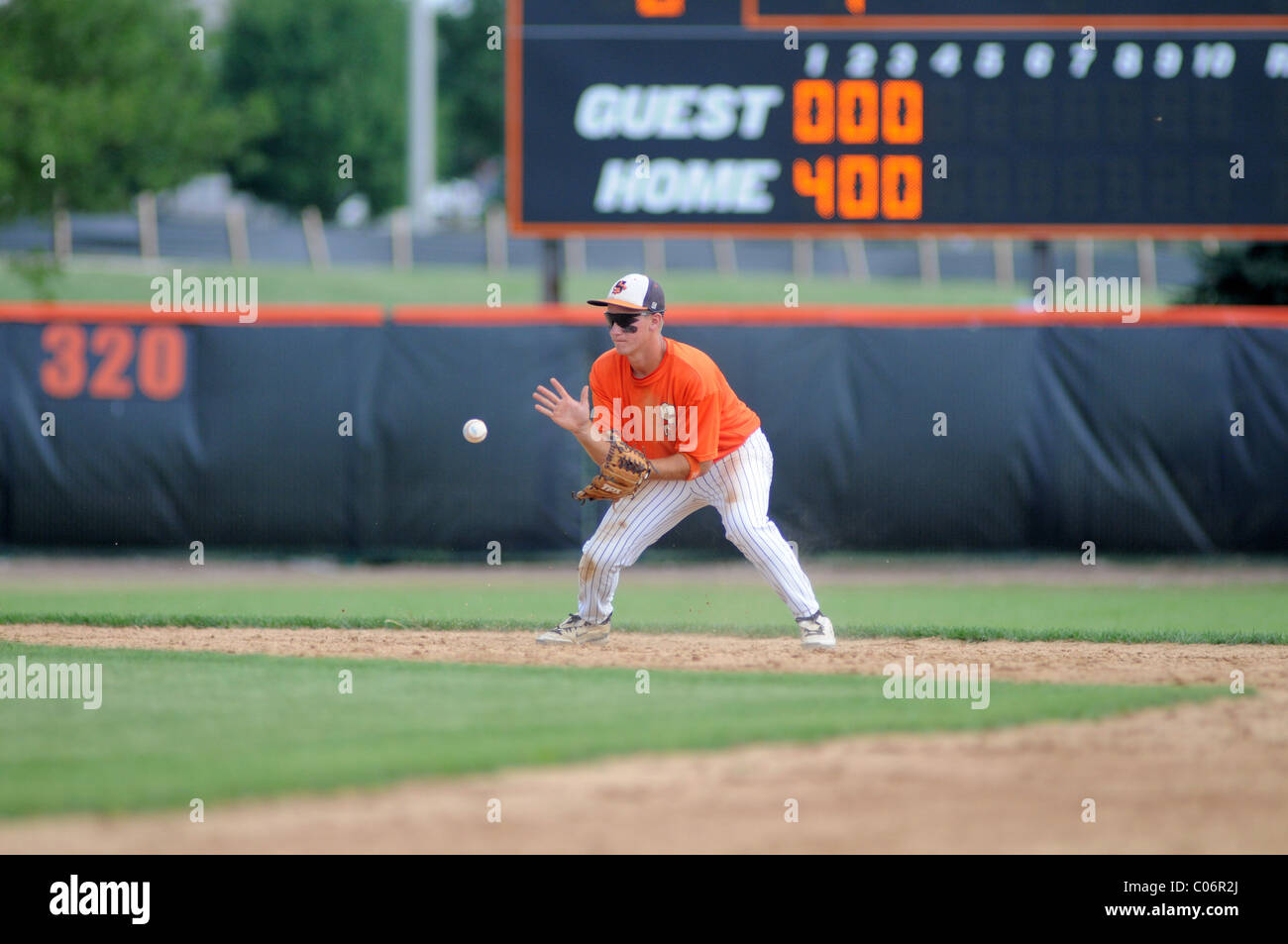 Les champs d'une balle au sol l'arrêt-court pendant un match de baseball de l'école secondaire avec son équipe de quatre pistes. USA. Banque D'Images