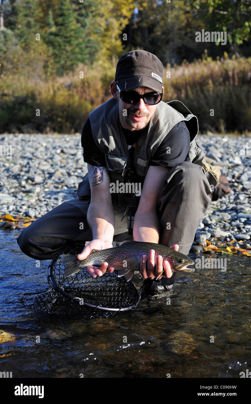Homme à genoux pour montrer un arc-en-ciel la truite pêchée dans la région de Deep Creek, péninsule de Kenai, Southcentral Alaska, automne Banque D'Images