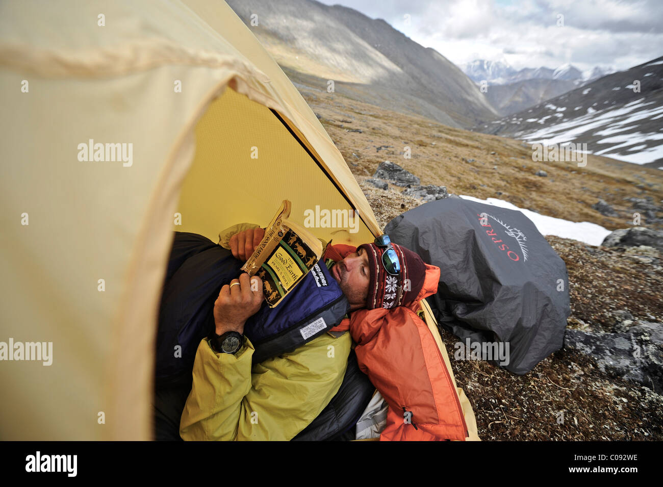 Backpacker lit un livre à l'intérieur d'une tente et attend le mauvais temps à un camp alpin Mt ci-dessous. Chamberln, Brooks, RFNA Banque D'Images