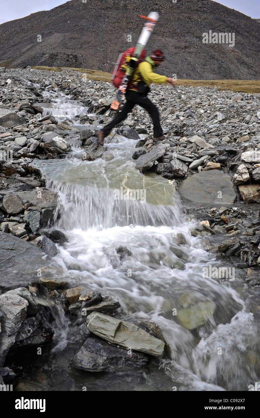 Backpacker traverse un ruisseau dans la vallée du ruisseau Katak revenant de Mt. Descente à ski Chamberlin, Brooks, RFNA Banque D'Images