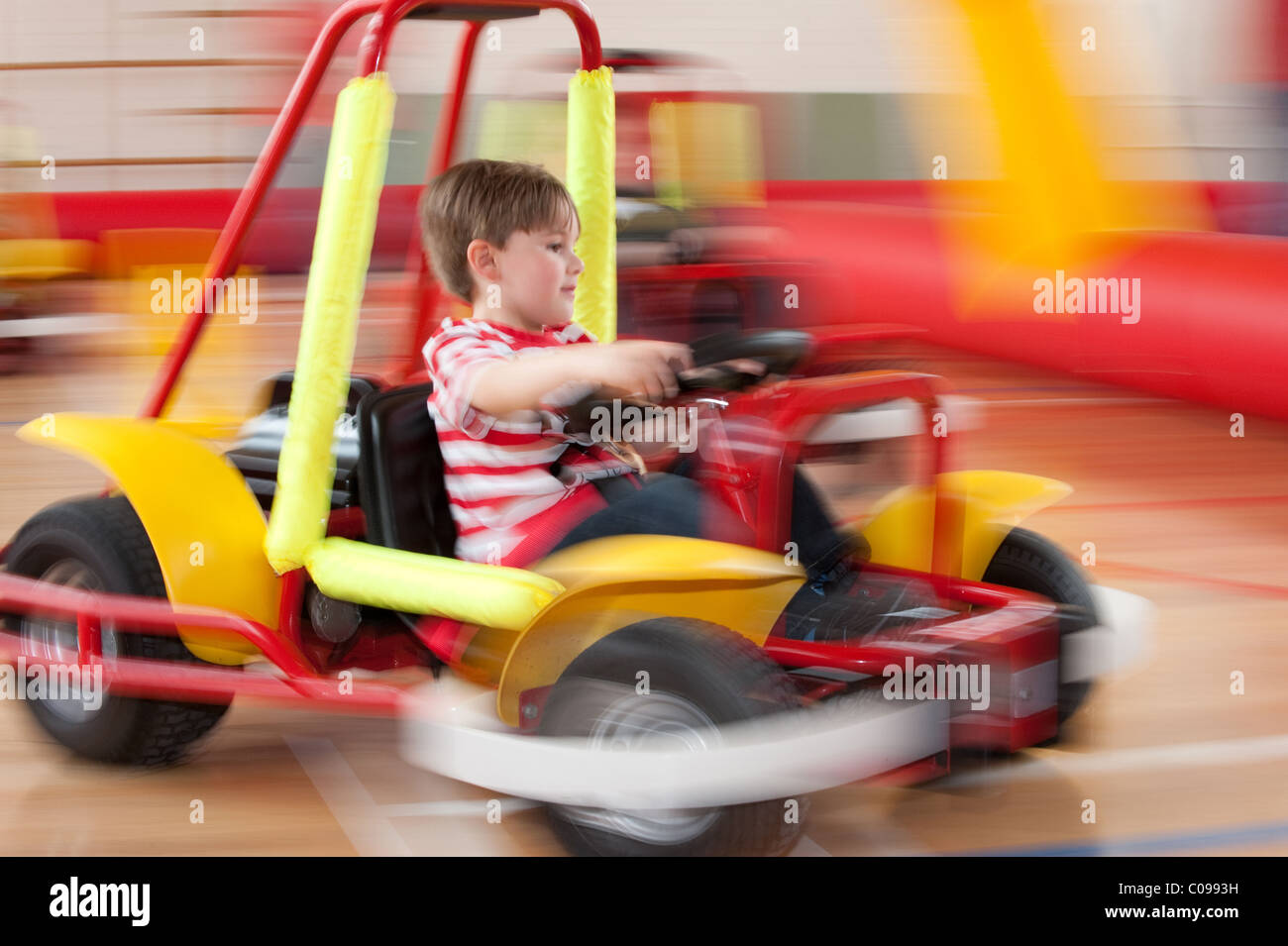 Une image floue de mouvement petit garçon au volant d'un kart pour enfants powered by autour d'une piste gonflable supervisé Banque D'Images