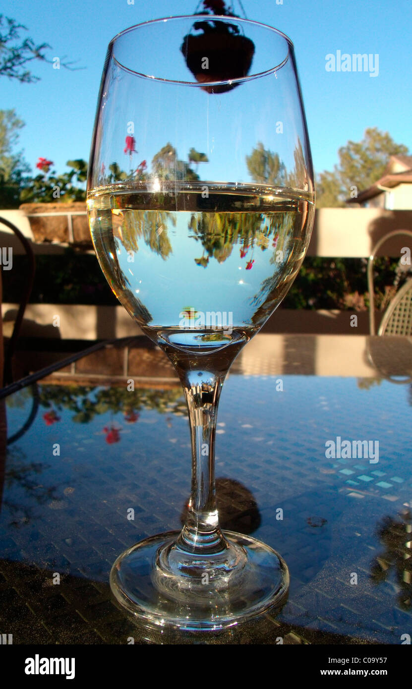 Verre de vin assis sur une table de patio en verre, chaud et ensoleillé l'après-midi d'été. Banque D'Images