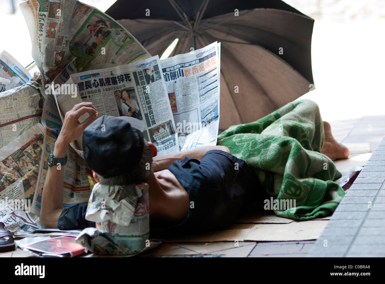 L'homme sans-abri qui s'est fait un très confortable et d'activité inventive à l'abri de carton, des journaux et un parapluie Banque D'Images