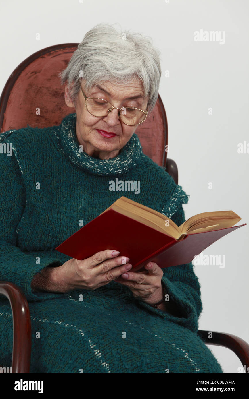 Portrait d'une vieille femme lisant un livre rouge sur fond gris. Banque D'Images