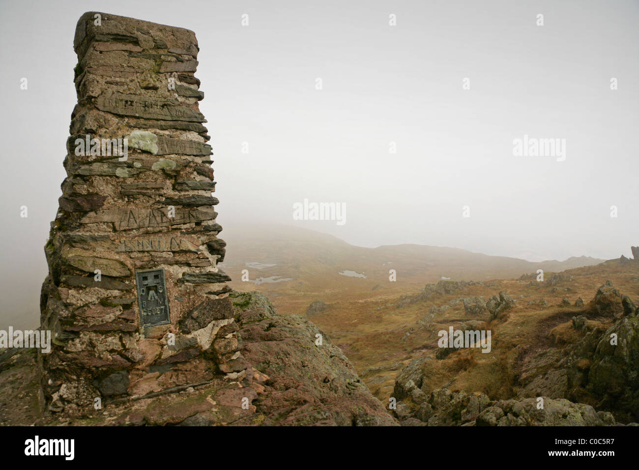 Cairn et Trig Point au sommet du lieu est tombé, Lake District, Cumbria, un jour nuageux. Banque D'Images