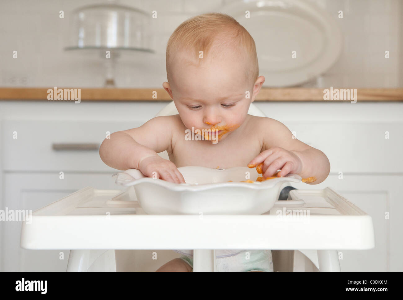 Messy baby eating dans une chaise haute Banque D'Images