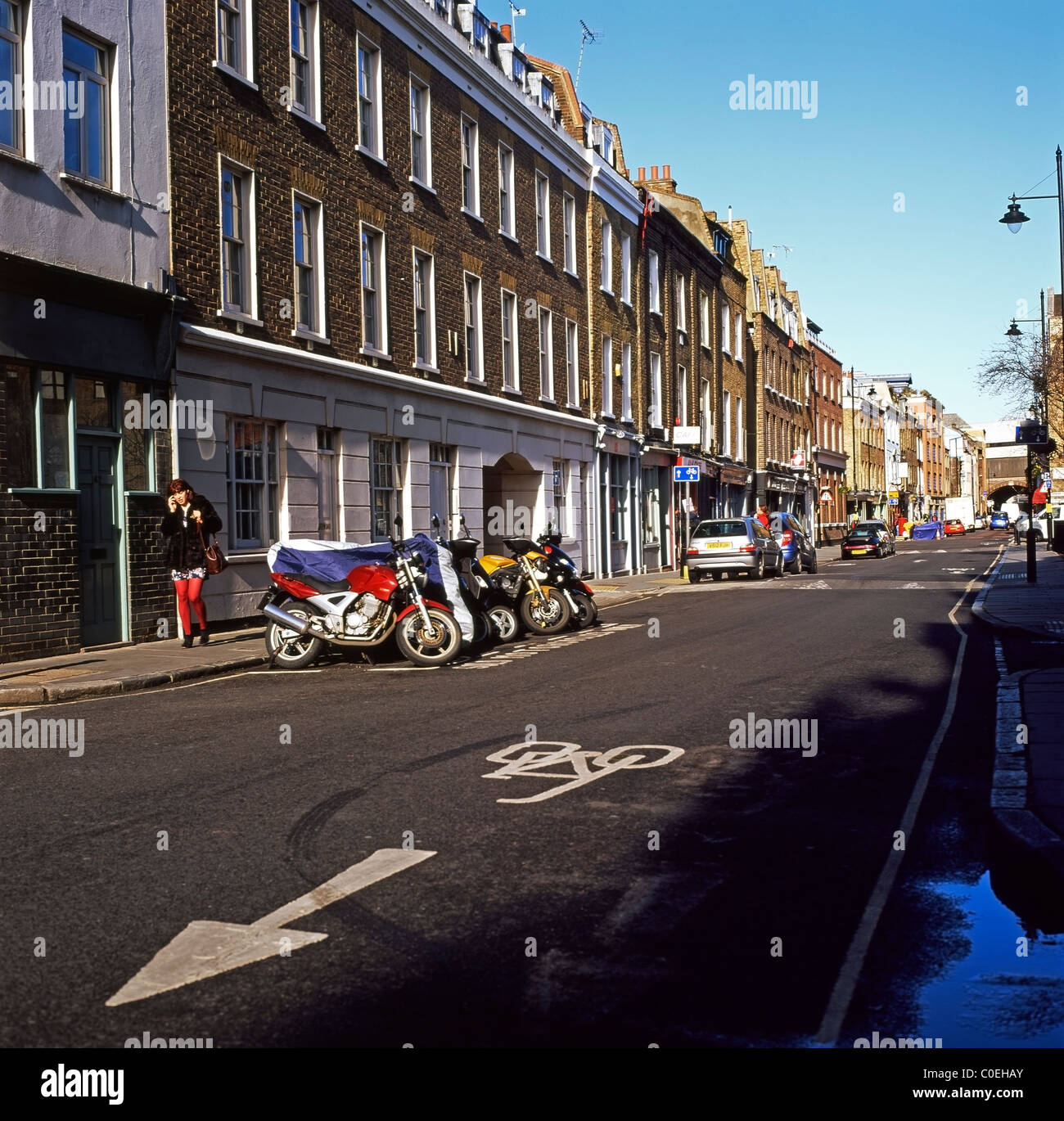 Une femme sur son téléphone portable en passant devant les motos en stationnement sur Bermondsey Street, South London SE1 England UK Banque D'Images