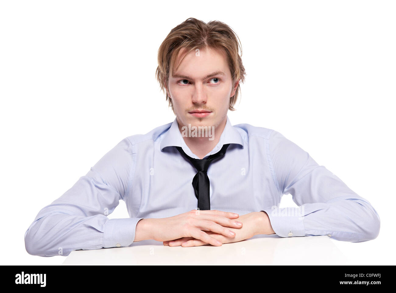 Jeune homme d'affaires, de travailleur ou étudiant assis à drôle de petite table. Studio photo, isolé. Banque D'Images