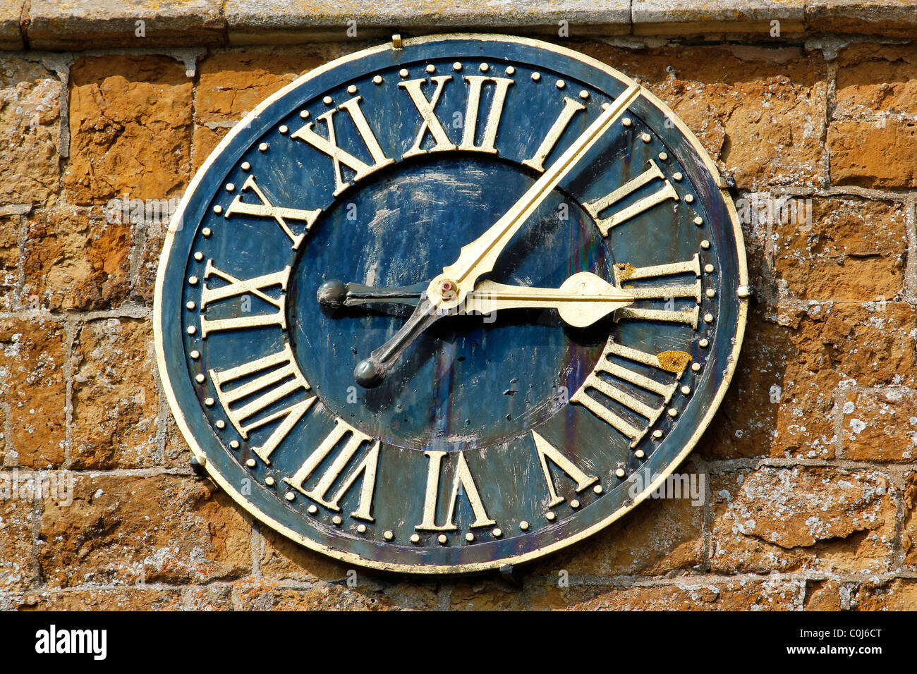 Horloge d'église ornée avec des chiffres romains sur la tour rustique moelleuse Ironstone de St. Peter's Church, Knossington, Leicestershire, Angleterre, Royaume-Uni Banque D'Images