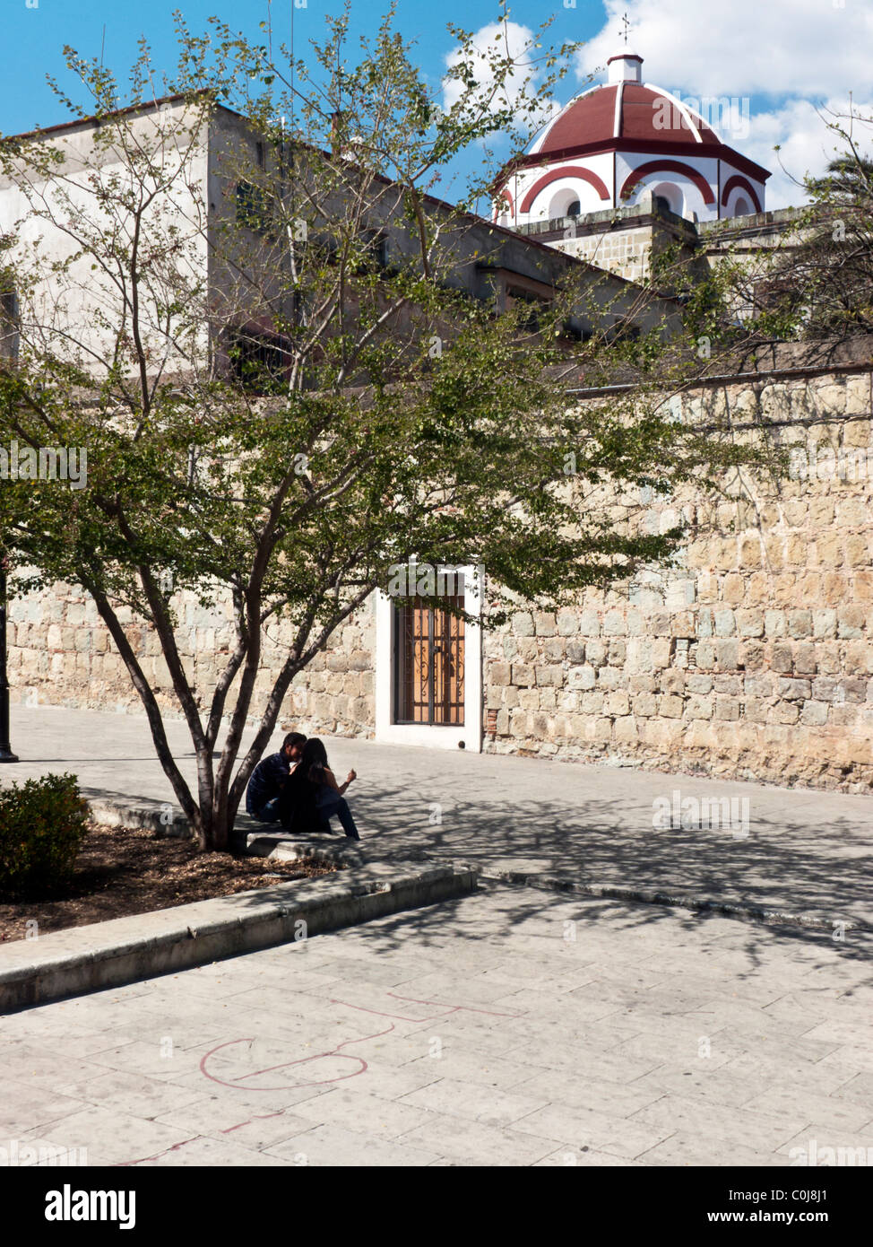 Couple de cour sous un arbre d'ombrage sur Plaza de Carmen Alto avec Dome de Carmen Alto visibles au-dessus de l'Église mur plaza Oaxaca Banque D'Images