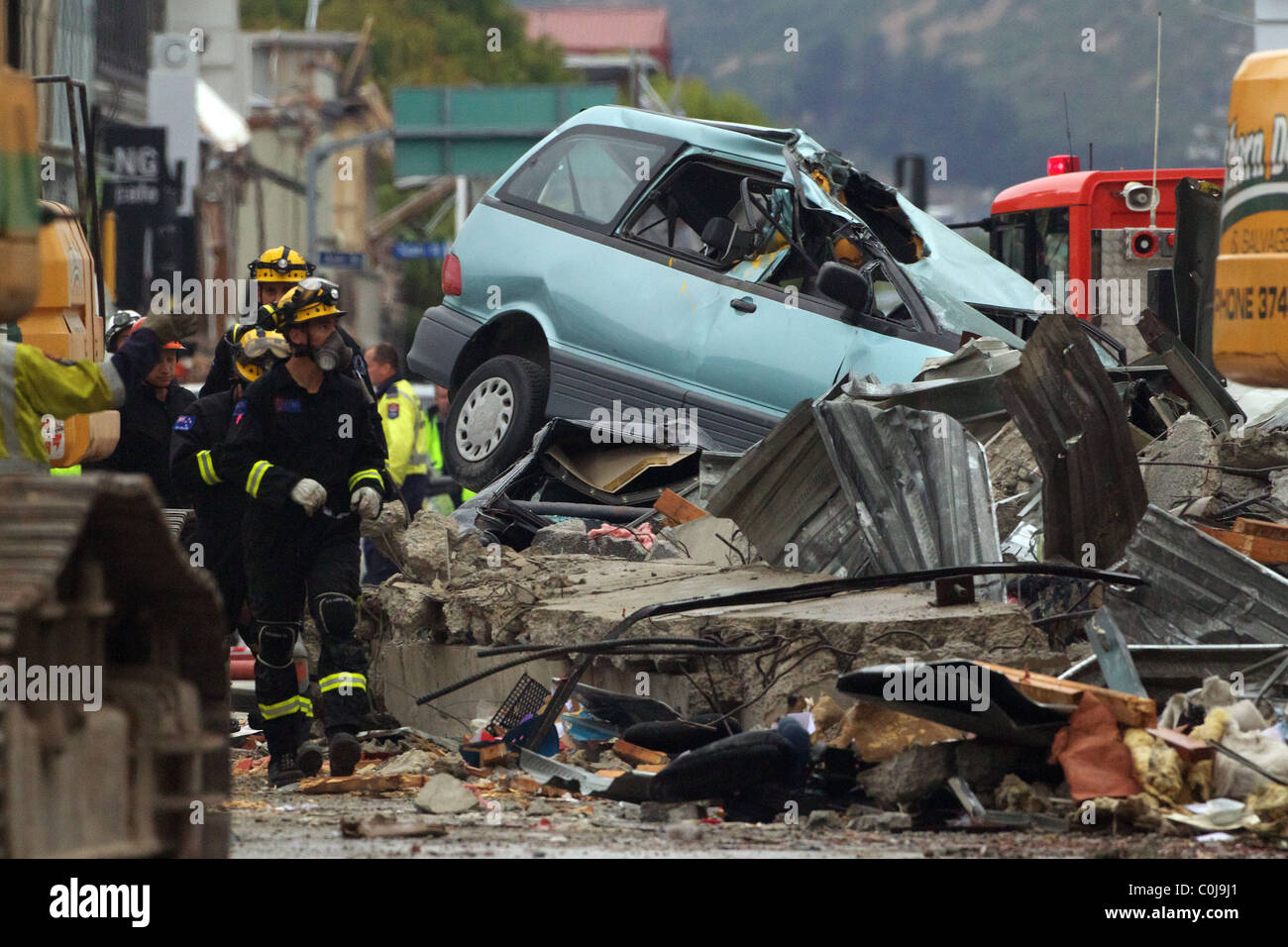 Les secouristes à pied passé voiture endommagée parmi les décombres dans le centre-ville après un puissant tremblement de terre a frappé Christchurch. Banque D'Images