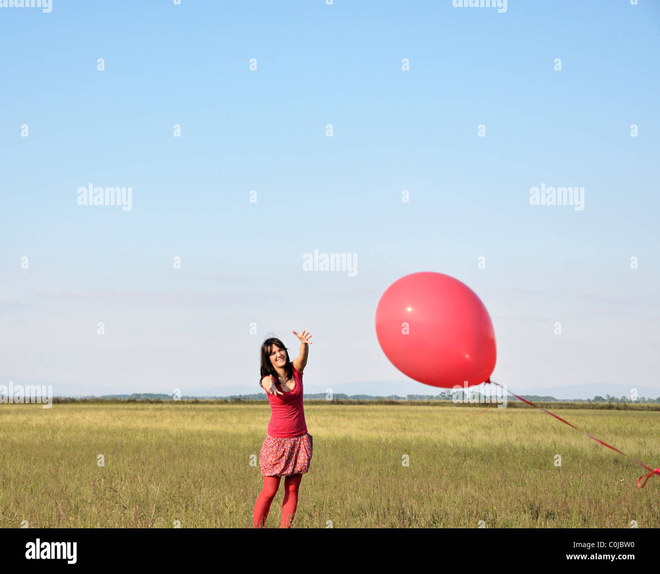 Young woman reaching for ballon rouge Banque D'Images