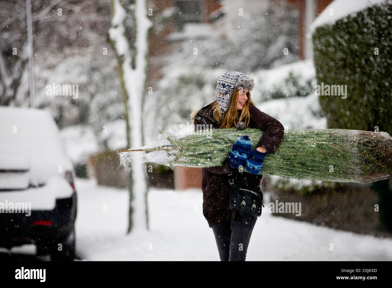 Une jeune femme portant un arbre de Noël le long d'une rue enneigée Banque D'Images
