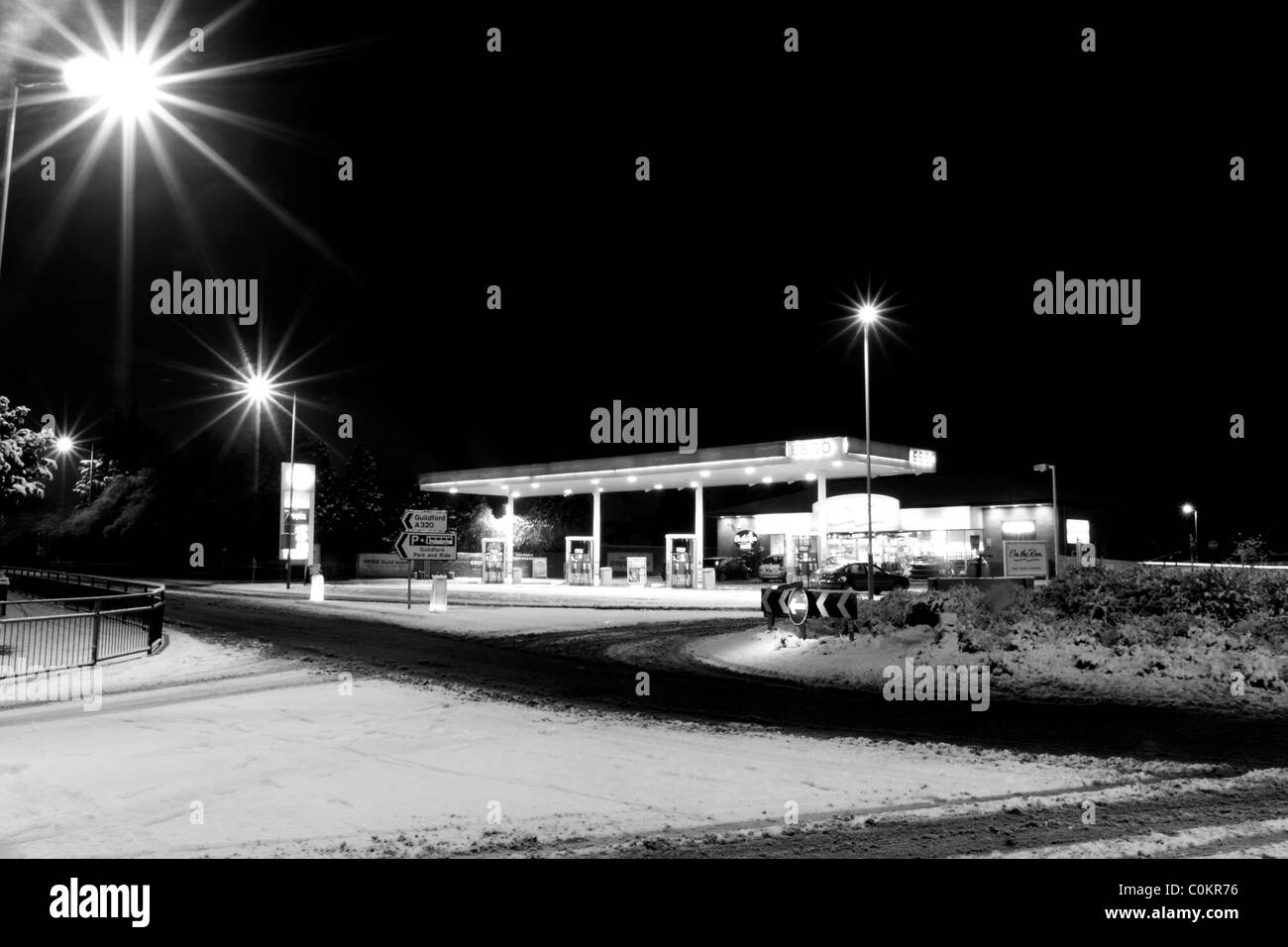 Une station essence à proximité d'un rond-point sur une route couverte de neige éclairé par des lumières de rue dans le noir. Banque D'Images