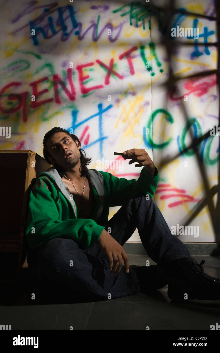 Toxicomane homme assis en face d'un mur couvert de graffitis Banque D'Images