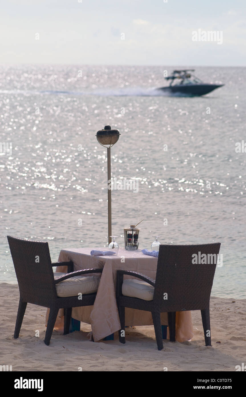 Un bateau de vitesse se précipite au-delà d'un dîner romantique pour deux sur la plage. Banque D'Images