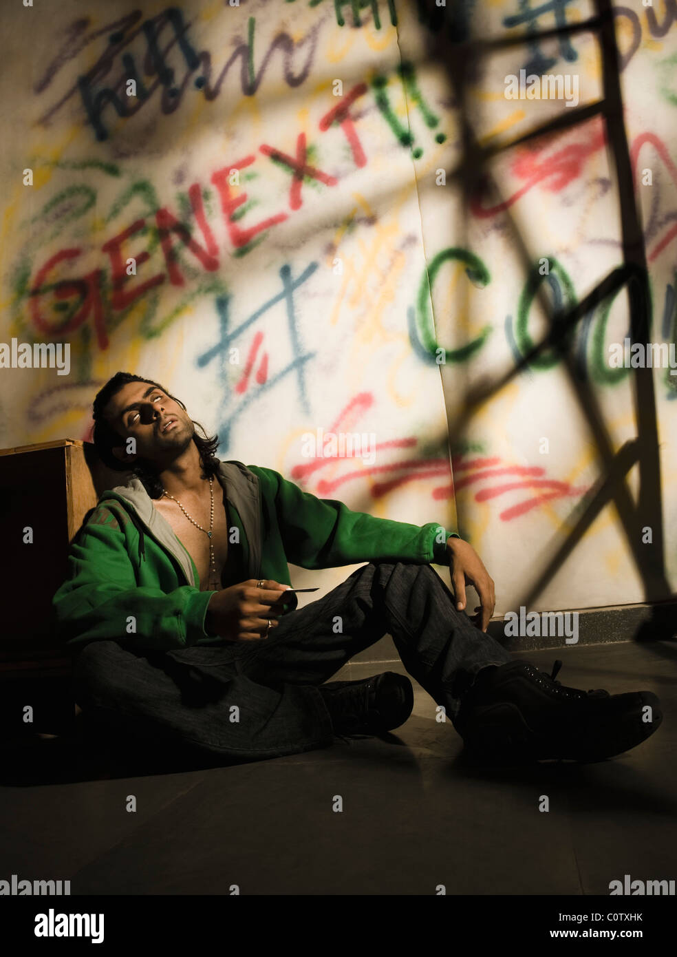 Toxicomane homme assis en face d'un mur couvert de graffitis Banque D'Images