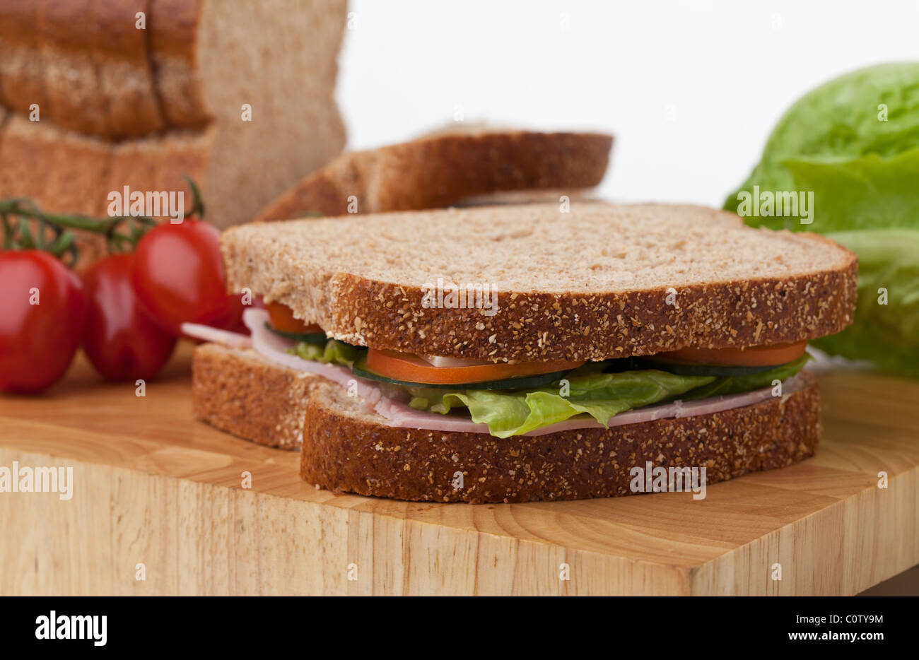 Salade de jambon et de sandwich complet fait maison sur une planche à découper, une miche de pain, les tomates et la laitue dans l'arrière-plan. Banque D'Images