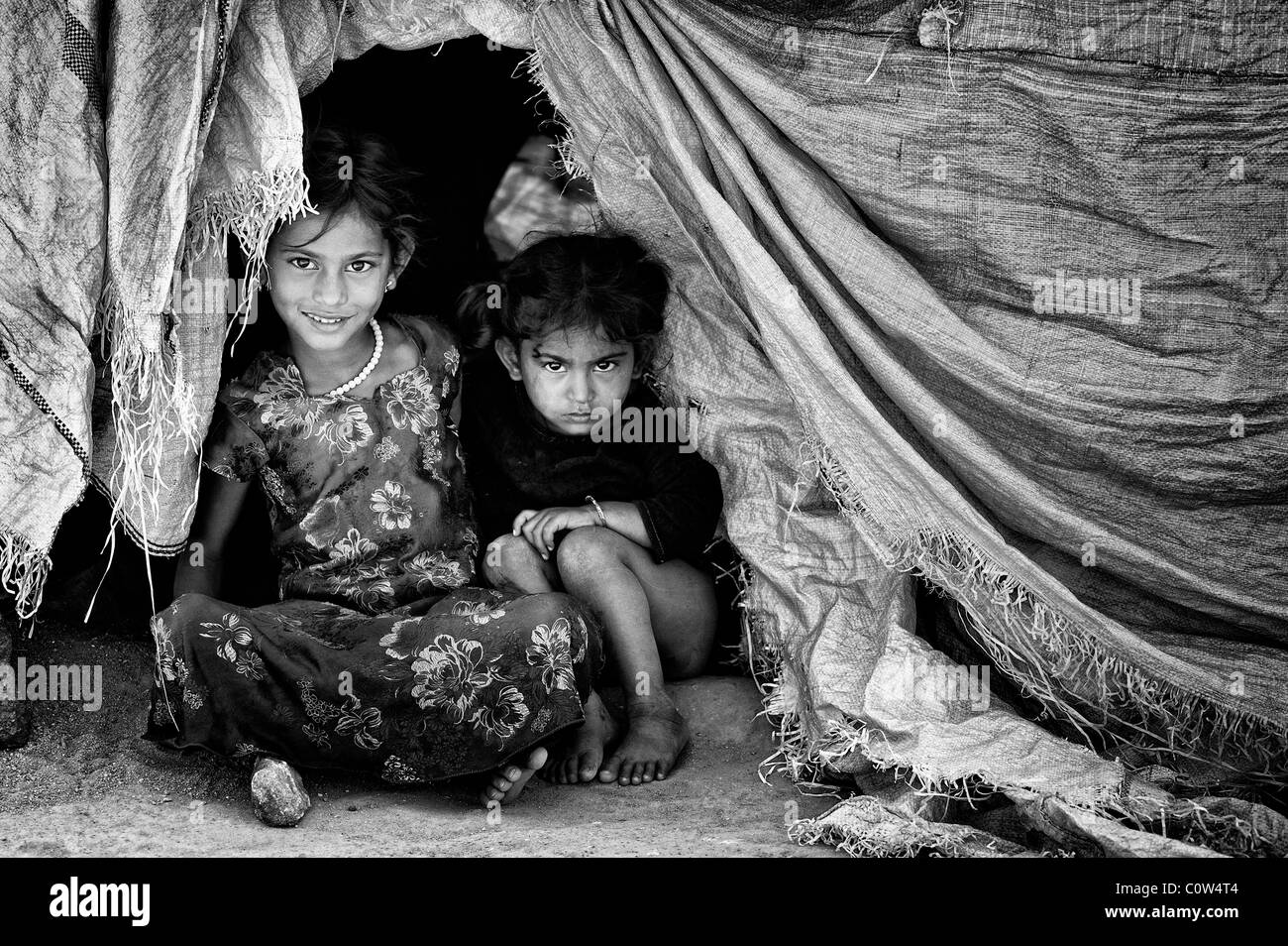 Les filles indiennes pauvres assis à l'entrée de la tente il y a la maison. L'Andhra Pradesh, Inde. Noir et blanc. Banque D'Images
