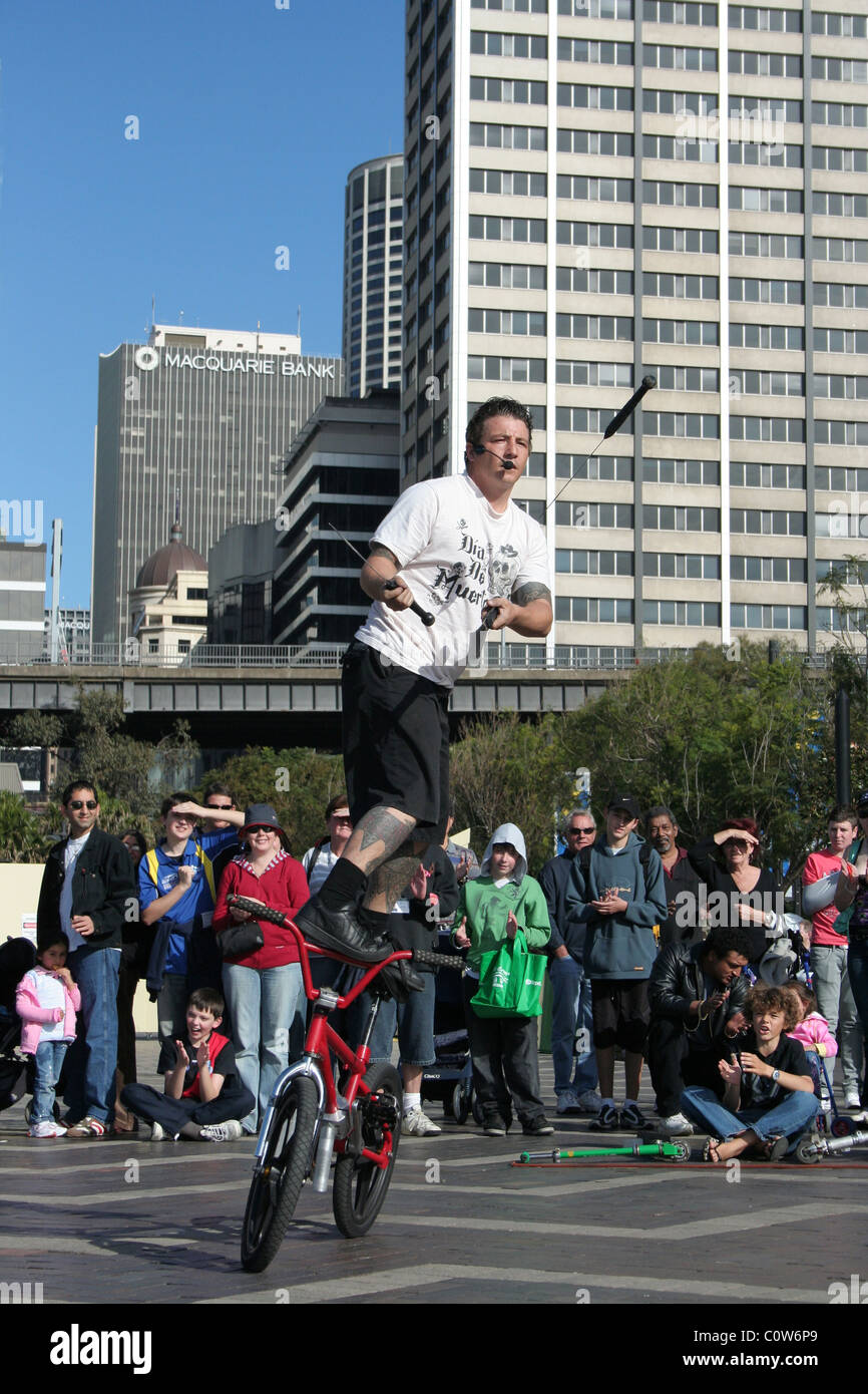 Artiste de rue balancing onhis vélo BMX tout en jonglant avec des torches de feu, la ville de Sydney, NSW, Australie Banque D'Images