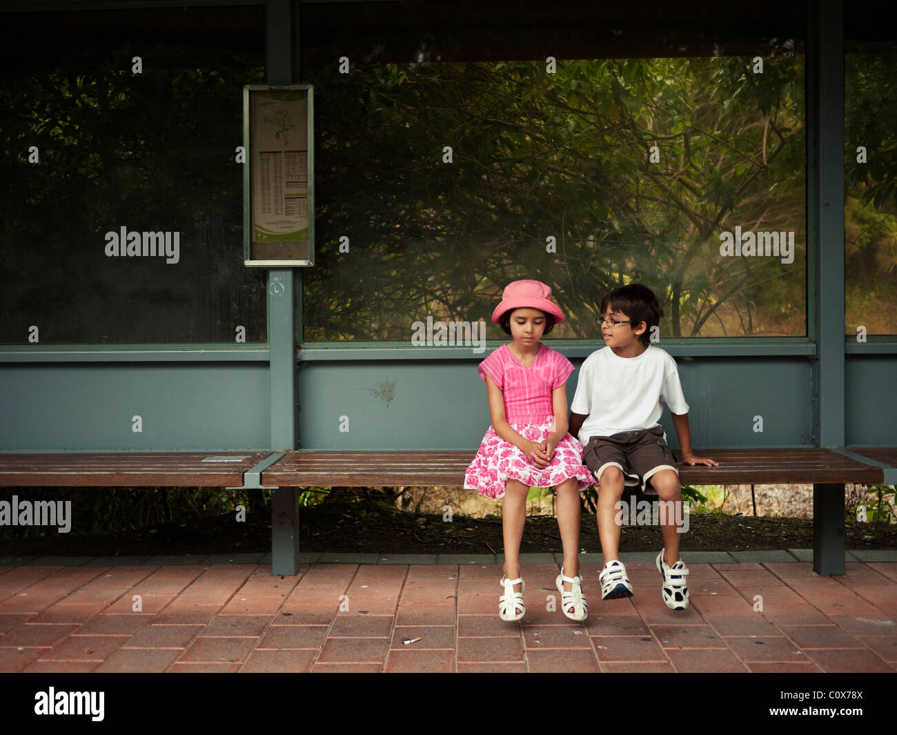 Garçon et fille s'asseoir sur un banc en attendant le bus. Banque D'Images