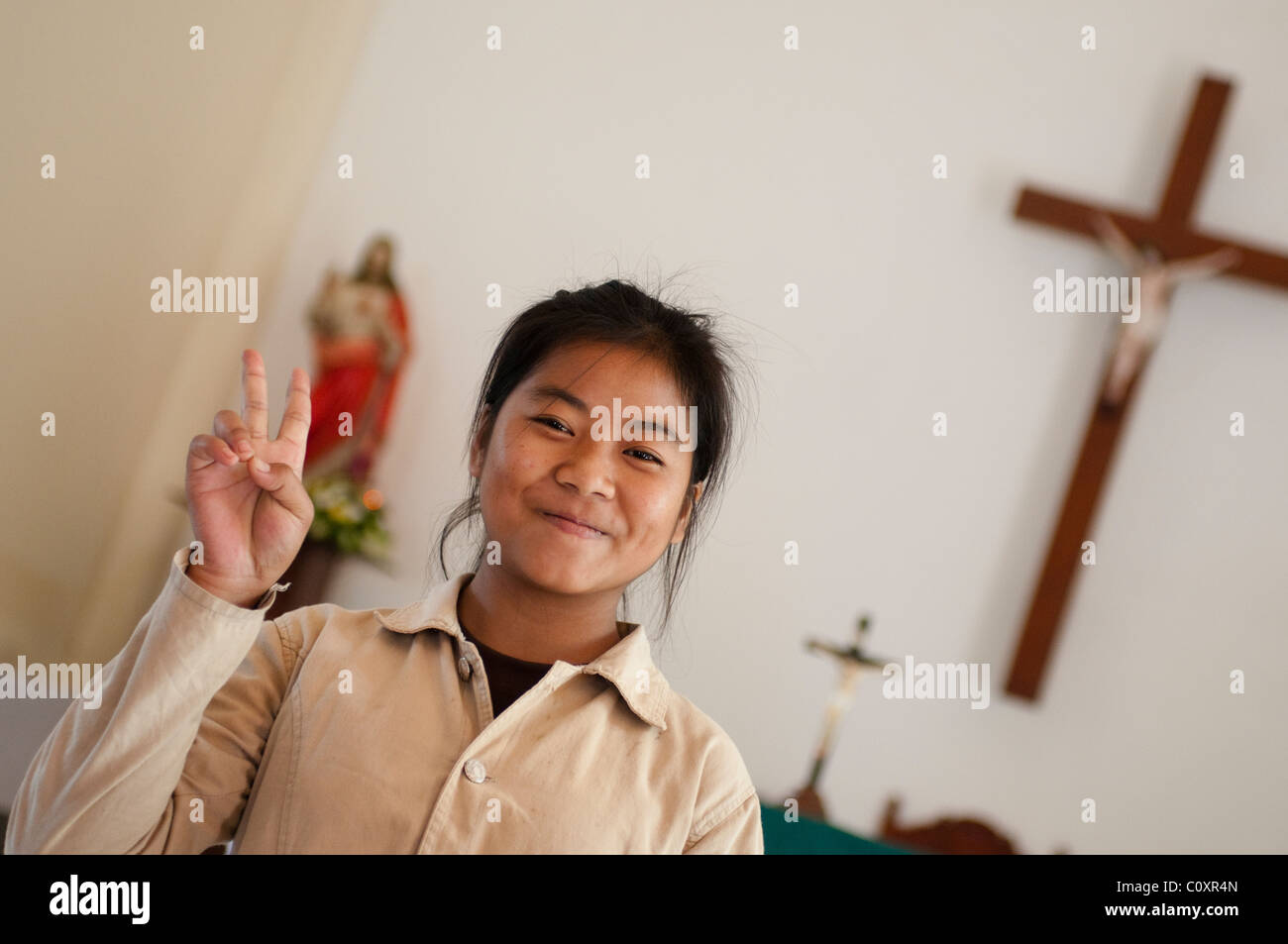 Smiling girl montrant la victoire dans l'église catholique Sainte Thérèse, Savannakhet, Laos Banque D'Images