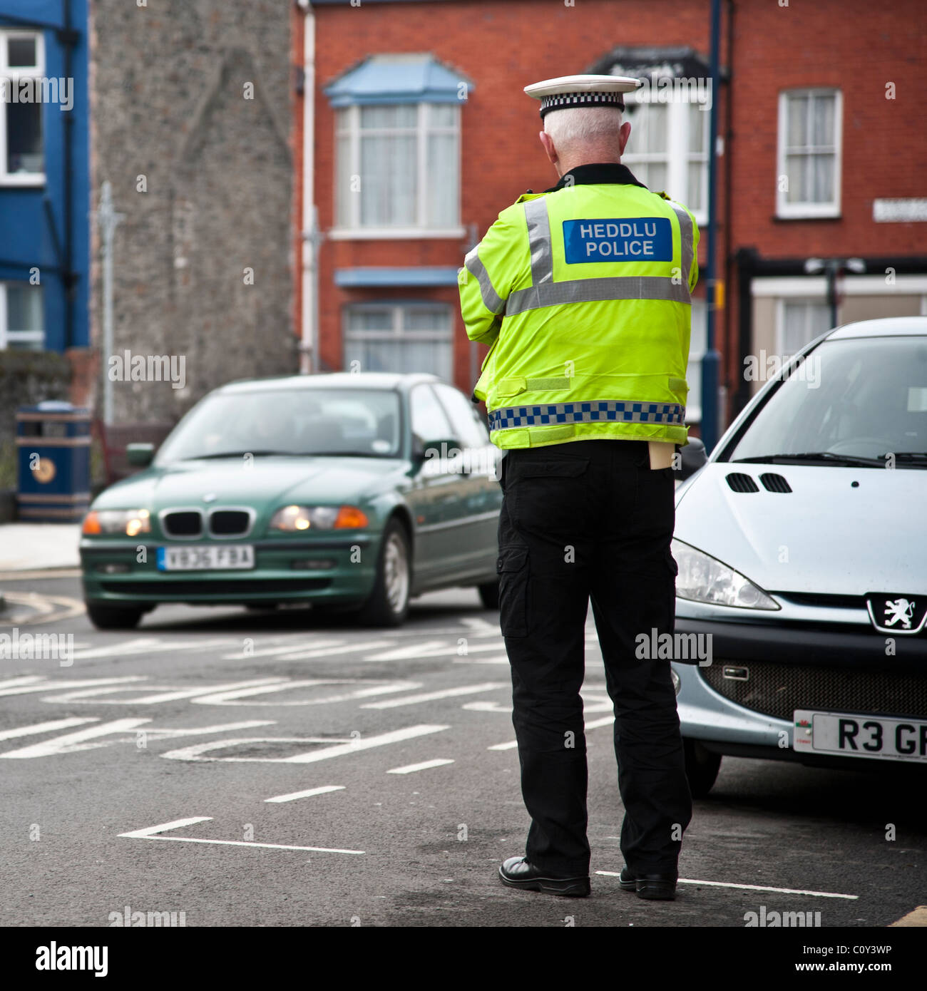 Vue arrière d'un agent de la circulation à regarder les voitures qui circulent sur une rue de ville, pays de Galles, Royaume-Uni Banque D'Images