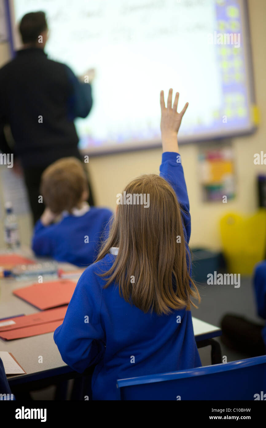 Groupe d'enfants en classe avec les mains en voulant répondre aux questions, le port de l'uniforme bleu Banque D'Images