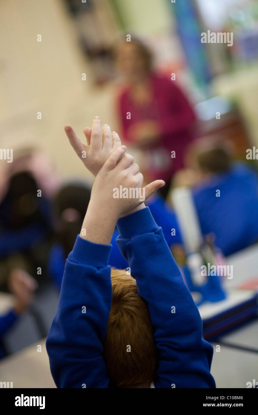 Groupe d'enfants en classe avec les mains en voulant répondre aux questions, le port de l'uniforme bleu Banque D'Images
