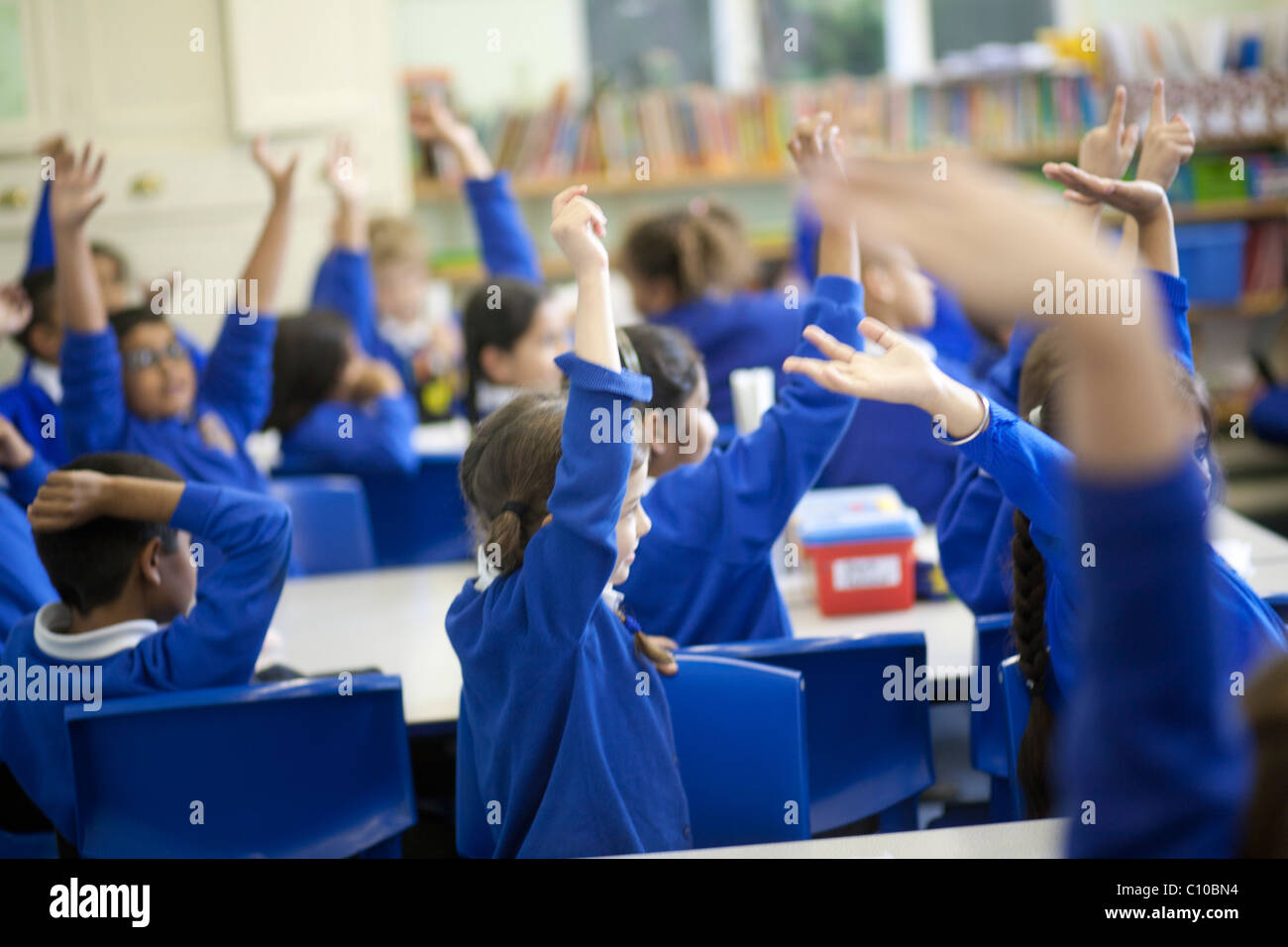 Groupe d'enfants en classe avec les mains en voulant répondre aux questions, le port de l'uniforme bleu Banque D'Images