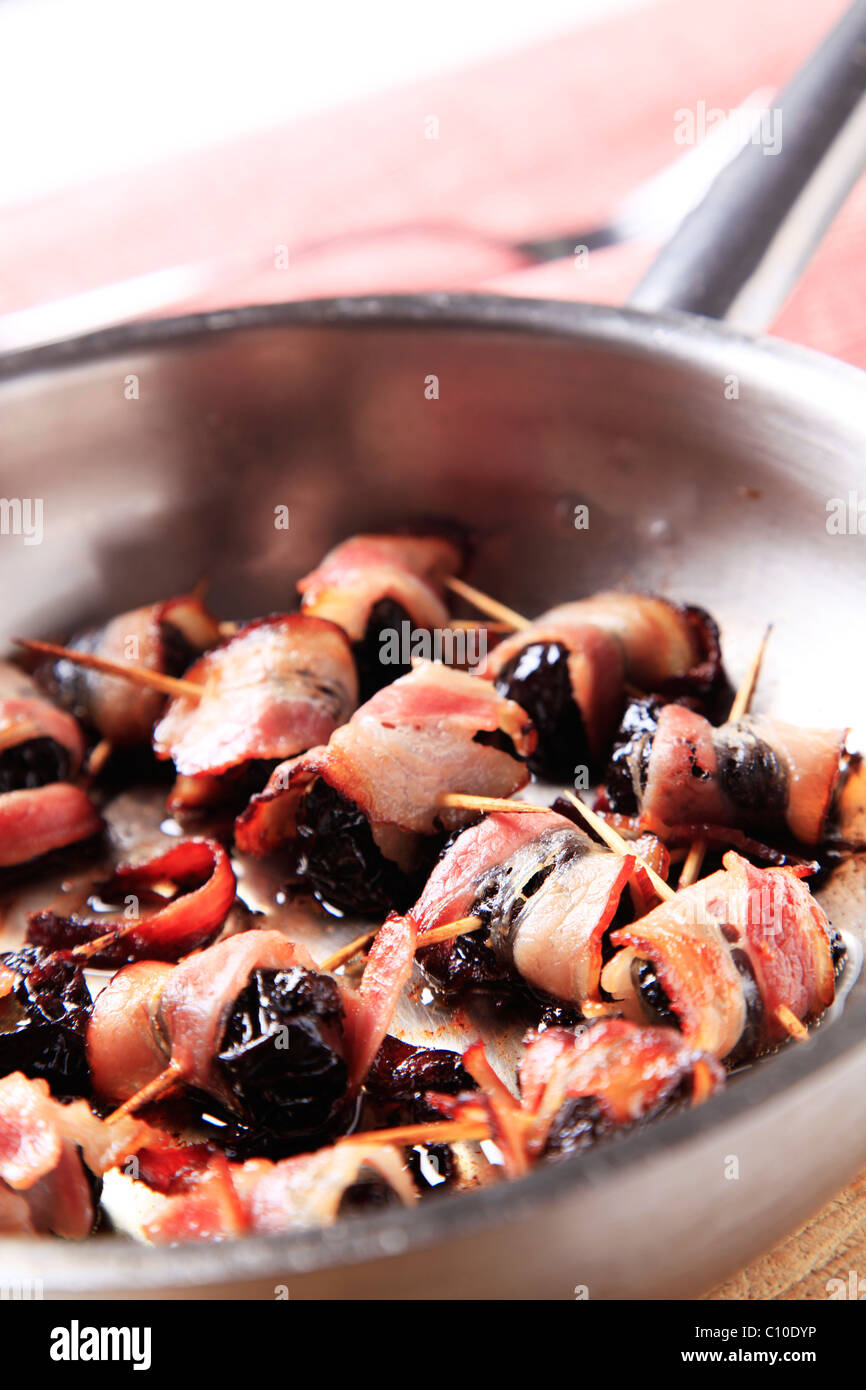 Pruneaux enroulés de bacon rôti pan étant - détail Banque D'Images