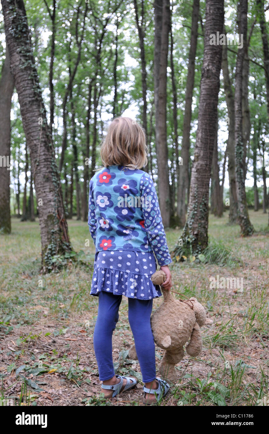 Une fillette de 8 ans, tenant son teddy-bear cherche dans woods Banque D'Images