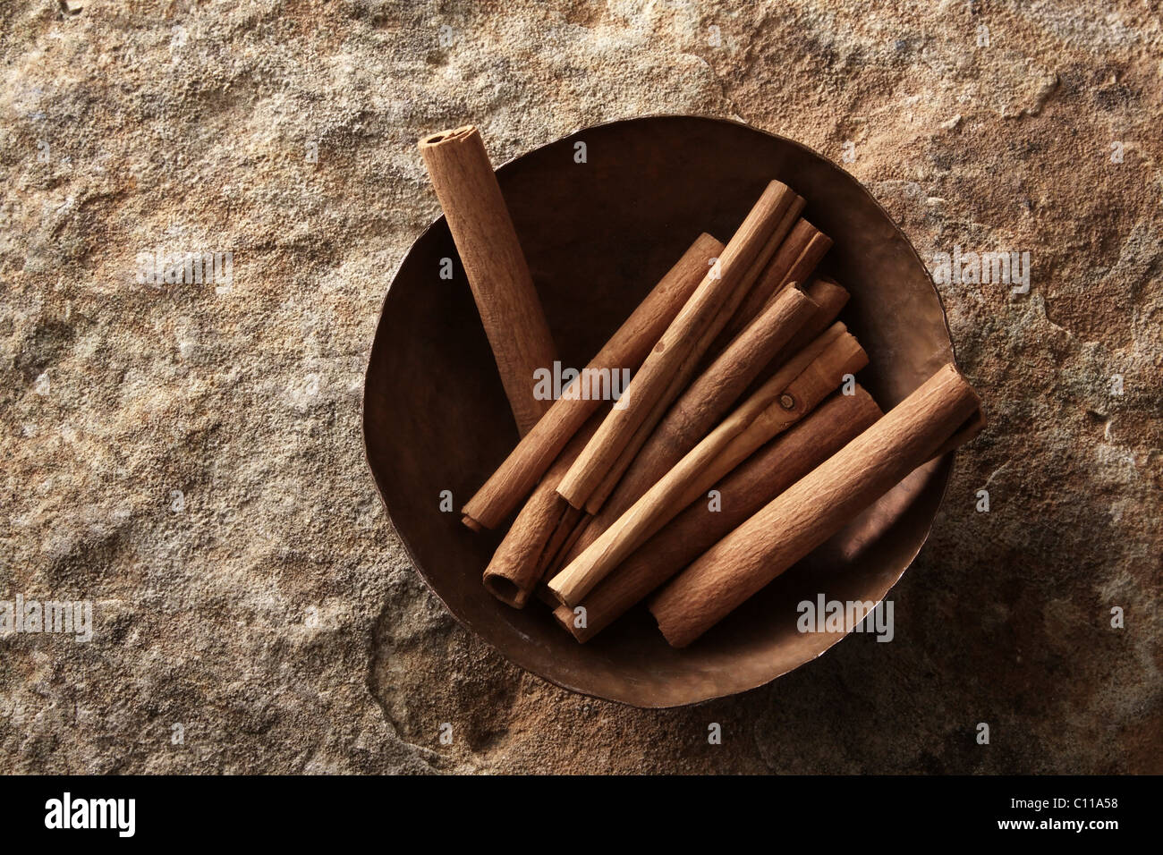 Bâtons de cannelle (Cinnamomum) dans un bol de cuivre sur une surface en pierre Banque D'Images