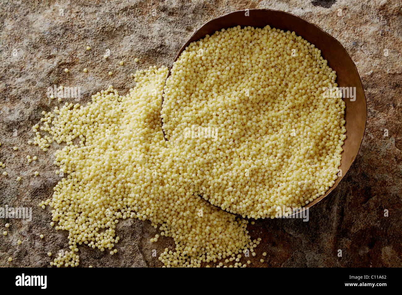 Millet (Panicum miliaceum) dans un bol de cuivre sur une surface en pierre Banque D'Images