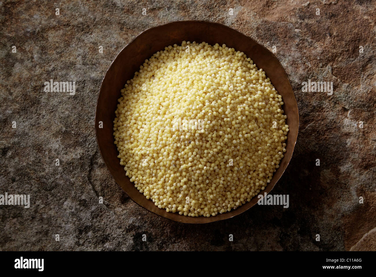 Millet (Panicum miliaceum) dans un bol de cuivre sur une surface en pierre Banque D'Images