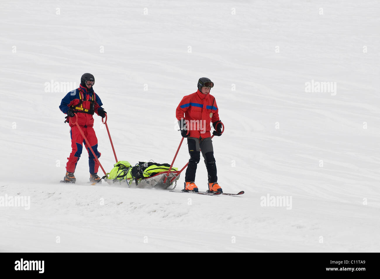 Service de secours en montagne à l'opération, deux secouristes sur les skis avec une civière de sauvetage ski dans la vallée, Chiemgau, Bavière Banque D'Images