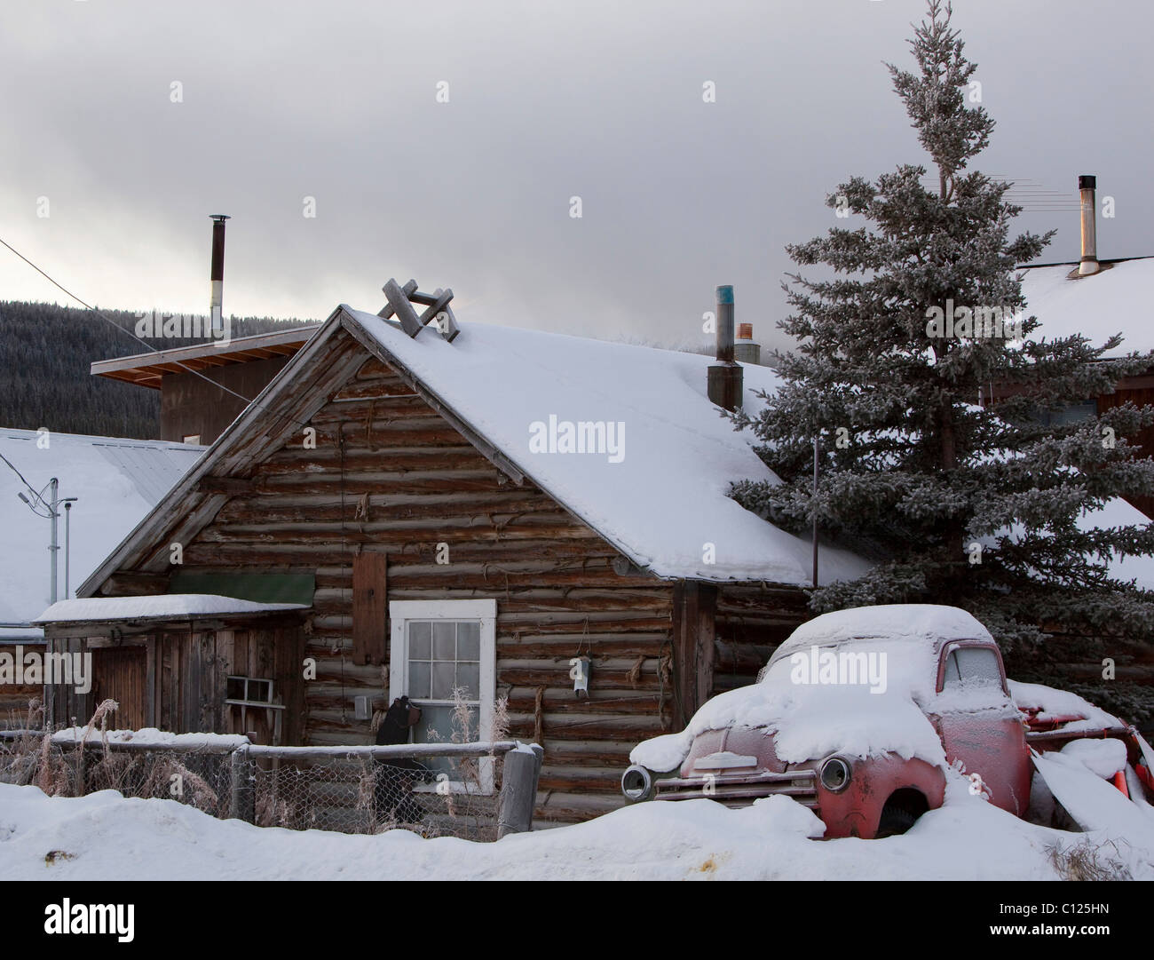 Vieille maison en bois et de vieux camions couverts de neige près du lac Bennett, Carcross, Territoire du Yukon, Canada Banque D'Images