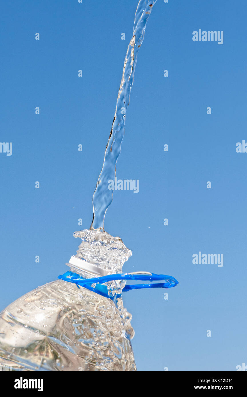 Verser de l'eau dans une bouteille d'eau minérale en plastique contre un ciel bleu Banque D'Images