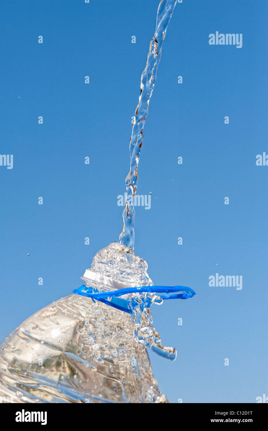 Verser de l'eau dans une bouteille d'eau minérale en plastique contre un ciel bleu Banque D'Images