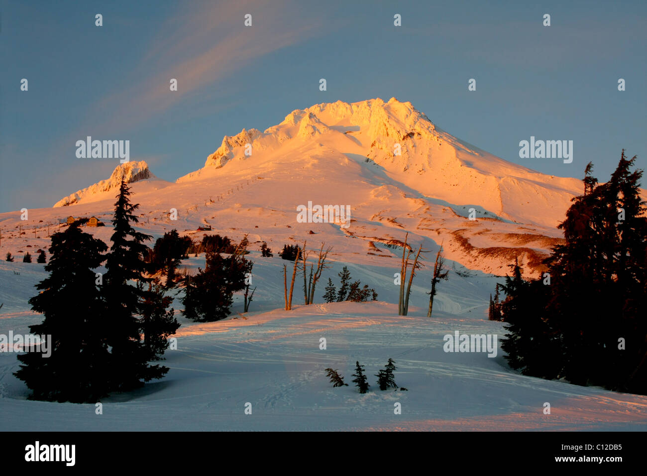 Un 40,171.06371la neige montagne déchiquetées en crête avec une lueur jaunâtre lumineux dans un coucher de soleil d'hiver blanc contre un ciel bleu Bébé doux. Banque D'Images