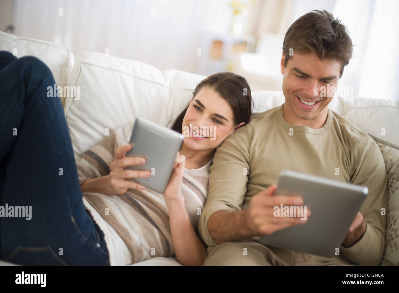 USA, New Jersey, Jersey City, Couple sitting on sofa, à l'aide de tablettes numériques Banque D'Images