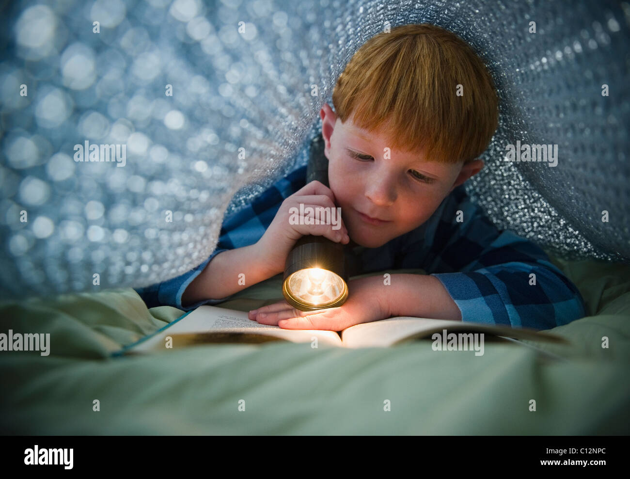 USA, New Jersey, Jersey City, Boy (8-9) reading book sous les couvre-lits Banque D'Images