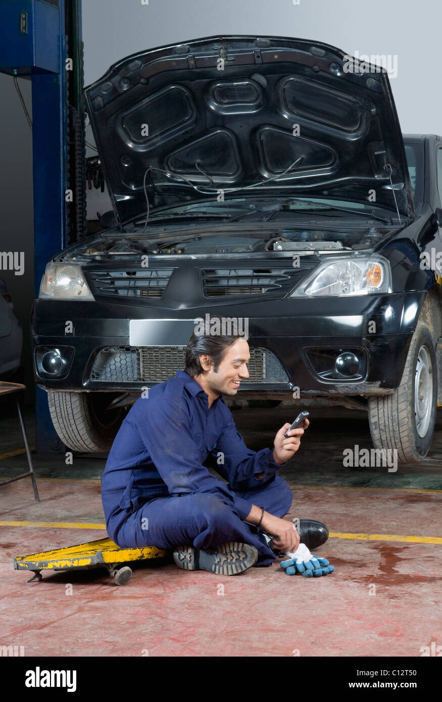 Mécanicien d'automobile à l'aide d'un téléphone mobile dans un garage Banque D'Images