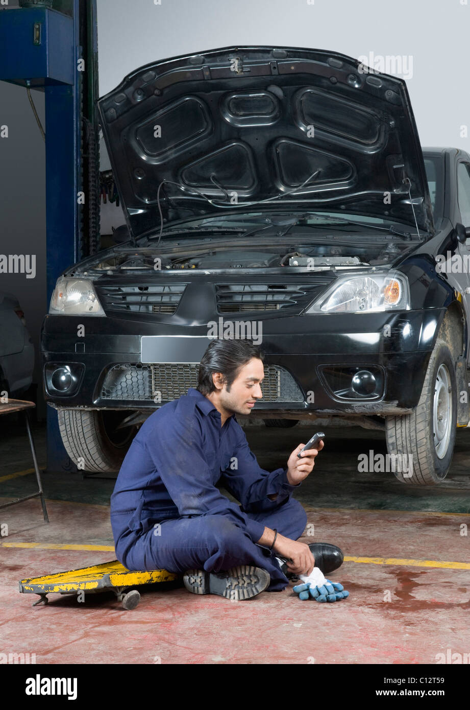 Mécanicien d'automobile à l'aide d'un téléphone mobile dans un garage Banque D'Images