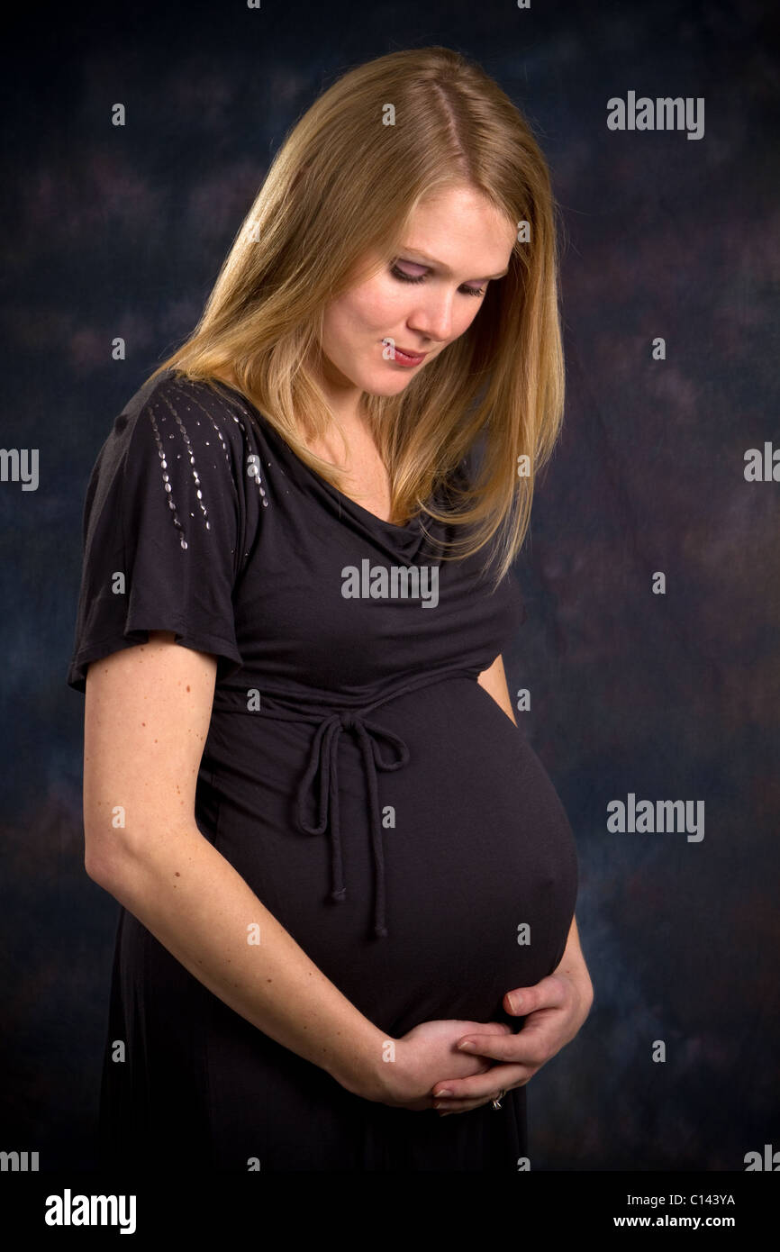 Future maman blonde dans le troisième trimestre de la grossesse tient son abdomen et regarde vers le bas en contemplant son enfant à naître. Banque D'Images