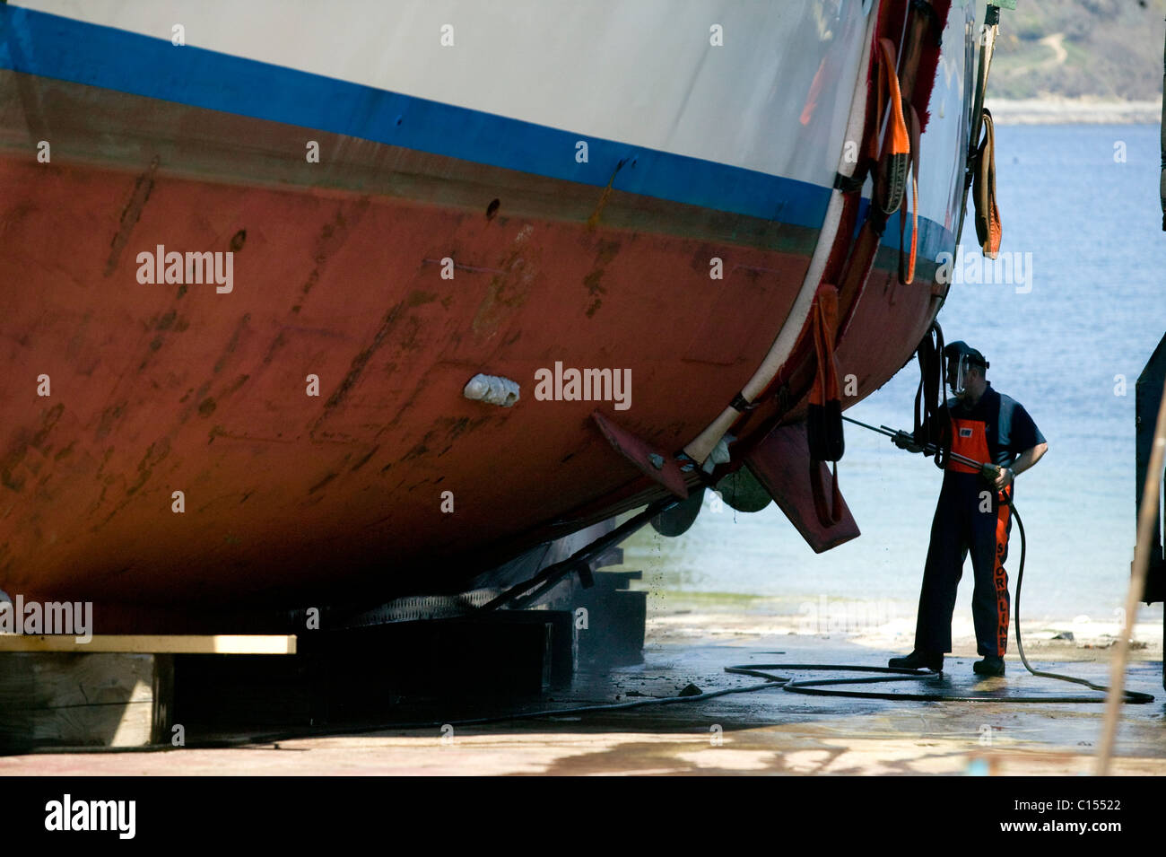 Un homme travaillant sur la coque d'un yacht sur la cale de halage au chantier Pendennis, Falmouth, Royaume-Uni Banque D'Images